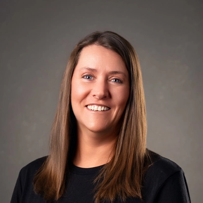 Staff Member Heather E Smiling In Front Of Grey Background
